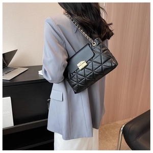 Detail of black quilted leather shoulder bag with gold chain strap and metal lock closure