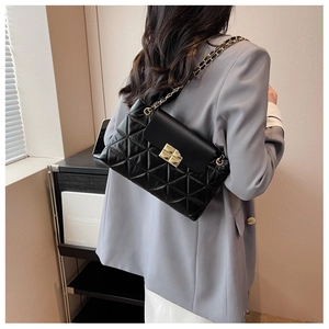 Detailed view of the black quilted chain bag featuring a gold clasp on a gray blazer