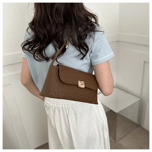 Modern brown woven leather baguette bag with a gold clasp shown worn by a model