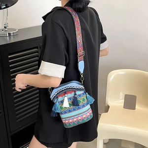 Ethnic embroidery bucket bag with colorful tassels and wide woven shoulder strap worn by model