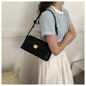 Detail of black woven shoulder bag with gold metal lock buckle and knotted strap accents