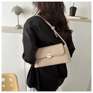 Detail of beige quilted shoulder bag with gold metal clasp on model in minimal setting