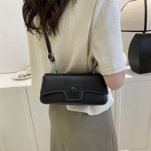 Minimalist black crossbody bag with white stitching shown on person in a clean home setting