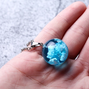 Blue sky and white cloud glass sphere pendant necklace with silver chain held in hand