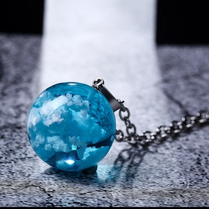Macro close-up of blue resin sphere pendant with cloud design on dark textured stone