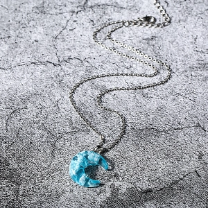 Detailed close-up of a silver crescent moon necklace featuring a blue sky and white cloud pendant