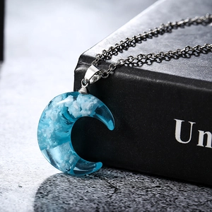 Detailed close-up of blue resin moon pendant necklace with white cloud texture