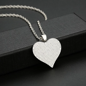 Polished silver heart pendant necklace with textured finish on a black grid jewelry box