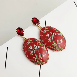 Macro detail of red oval acrylic drop earrings featuring exquisite floral and bird patterns