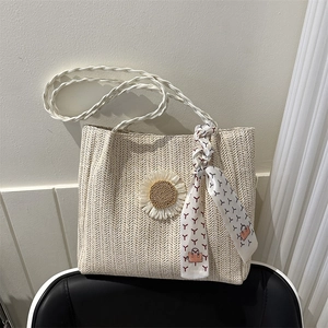 Sac fourre-tout en paille avec breloque tournesol et foulard en soie sur une chaise