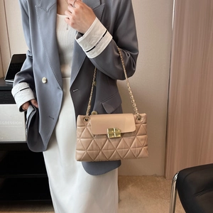 Elegant beige quilted chain bag with gold hardware worn over a stylish white dress