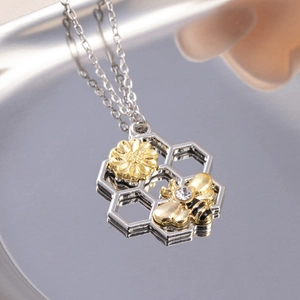 Silver honeycomb necklace with golden bee and flower accents on a mirror tray