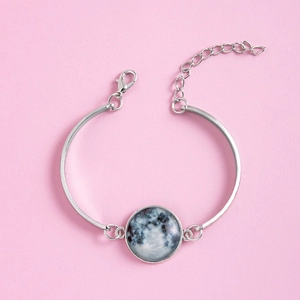 Détail du bracelet réglable en argent avec pendentif dôme en verre lune sur fond rose