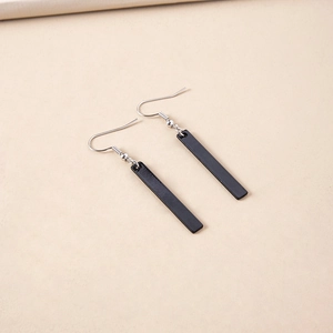 Minimalist black rectangular drop earrings with silver fish hook ear wires on beige background
