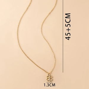 Vue détaillée du pendentif trèfle doré avec chaîne de 45+5cm sur fond pêche doux
