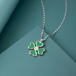 Gros plan du collier trèfle à quatre feuilles vert avec chaîne argentée sur fond géométrique