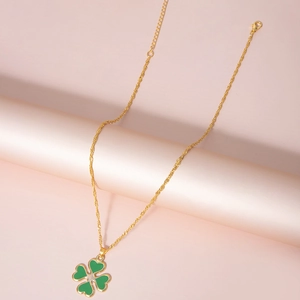 Vue détaillée de la chaîne dorée et du pendentif trèfle vert sur un support rose doux