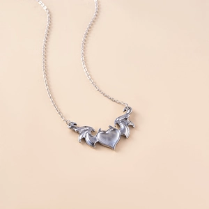 Close-up of gothic devil wings and heart pendant on a delicate silver link chain