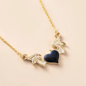 Macro detail of gothic devil wing necklace with black heart pendant and gold chain