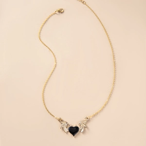Macro detail of gothic devil wing pendant featuring black heart enamel and gold finish