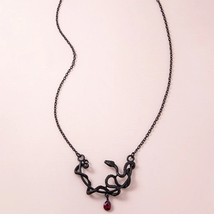 Retro black snake pendant necklace with a red teardrop gemstone on a minimal background