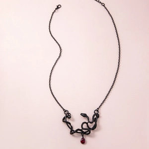 Gothic black snake pendant necklace with a red teardrop stone on pink background