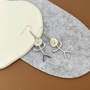 Détail des boucles d'oreilles bonhomme allumette argentées avec geste du majeur sur assiette