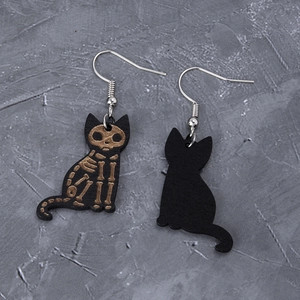 Detail of gothic black wooden earrings with carved cat skeleton design and silver hooks