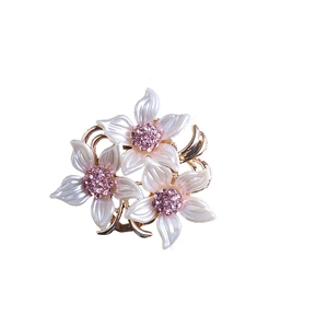 Broche fleur dorée élégante avec pétales blanc perle et cristaux roses sur fond blanc