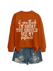 Flat lay of an orange crewneck sweatshirt with slogan and distressed denim shorts