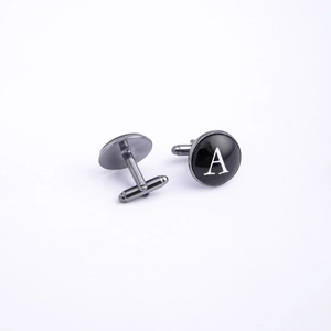 Macro detail of gunmetal cufflinks featuring a white letter A and T-shape closure