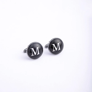 Detail of round gunmetal cufflinks featuring black enamel and white letter M engraving