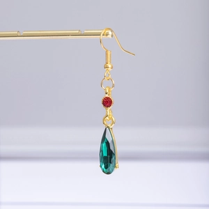Detailed macro view of the gold hook earring featuring red round and green teardrop gems