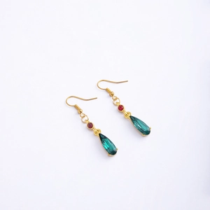 Detail of anime style gold earrings featuring red gems and green teardrop glass pendants