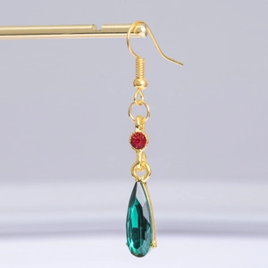 Macro view of Howl's emerald green waterdrop earrings with gold hooks and red gems