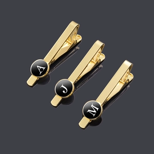 Polished gold initial necktie clips with black circular letter A, J, M in a modern style