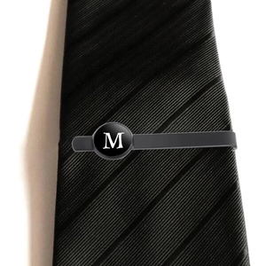 Men's premium black stainless steel tie clip with white letter M on striped necktie