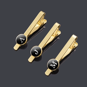 Detailed view of polished gold tie clips featuring black letter charms A, J, and M