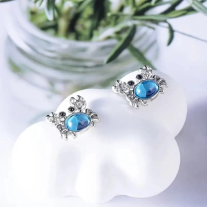 Silver crab earrings with blue opal and small crystals on a white cloud stand