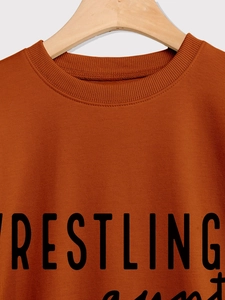 Detail of burnt orange crewneck sweatshirt showing ribbed collar and Wrestling print