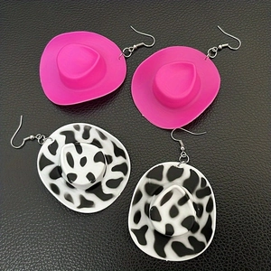 Pink and cow print cowboy hat earrings set on black textured background