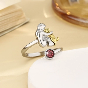 Macro shot of silver ring with gold girl hugging dog design and red gemstone detail