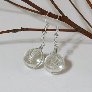 Minimalist clear glass ball earrings with dandelion seeds hanging on a branch