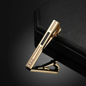 Men's gold tie clip with black enamel inlay and three crystals on a dark surface
