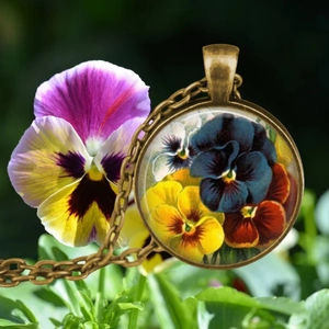 Gros plan d'un pendentif pensée en bronze sur fond de fleurs violettes naturelles
