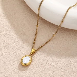 Detail einer goldenen Satellite-Kette mit einem ovalen Muschel-Anhänger auf feinem Sand