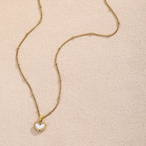 Detail der goldenen Satellitenkette mit Herz-Muschel-Anhänger auf beigem Hintergrund