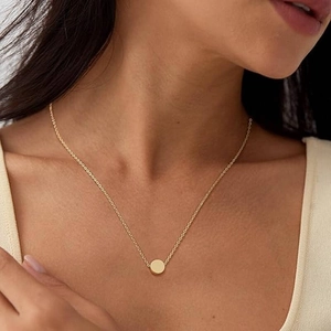 Detail of a minimalist gold necklace with round bead pendant worn on a model's neck