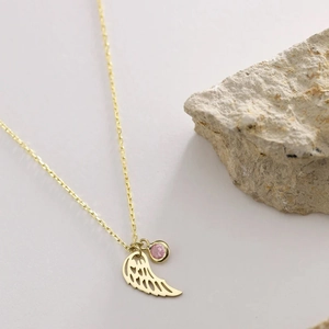 Detalle de colgante de alas de ángel doradas con piedra rosa sobre fondo de piedra natural