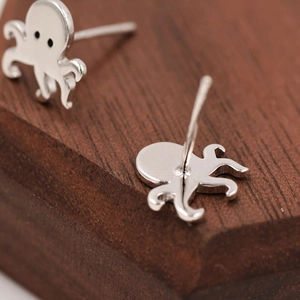 Detailed view of octopus stud earrings with white enamel finish on a wooden base